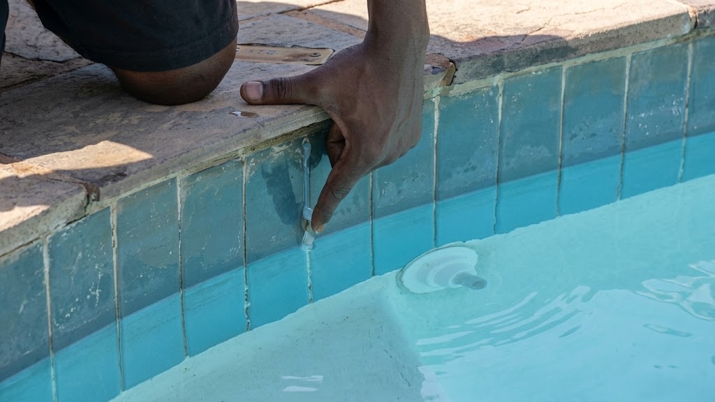 A yellow rubber duck placed on a brick surface near a blue swimming pool.